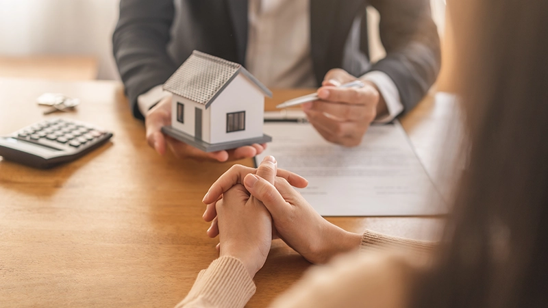 A real estate agent or lawyer, holding a small model of a house while talking to a client.