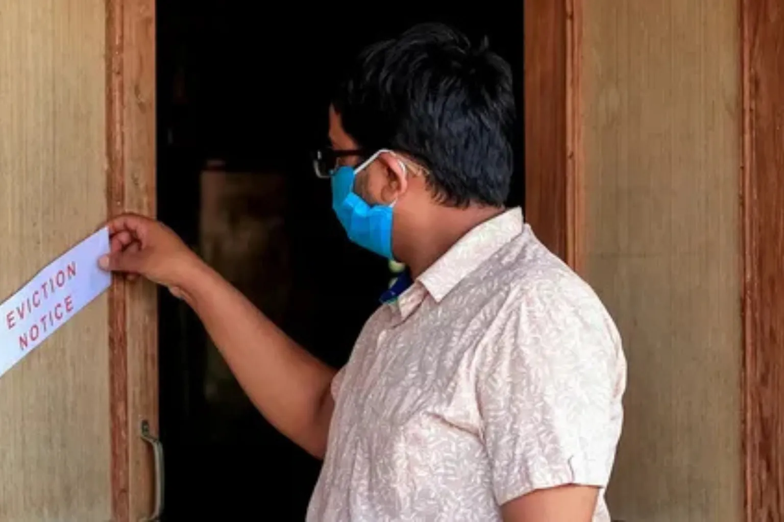 A man wearing a face mask holding a paper with the words ‘Eviction Notice.’